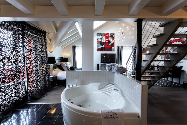 A modern hotel room with a large bathtub, a staircase, and a living area with a sofa and a TV.