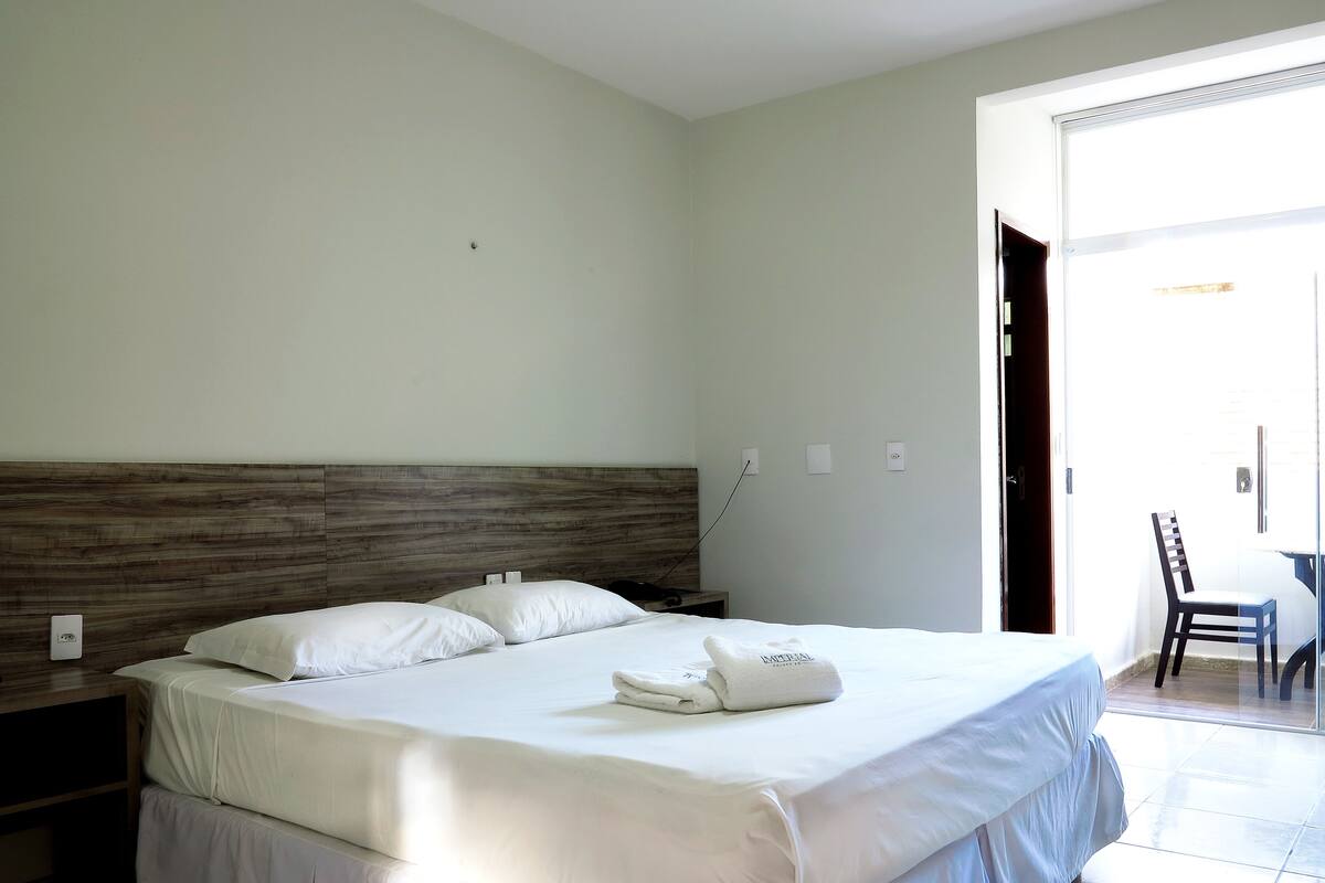 Ein Hotelzimmer mit einem großen Bett, einem hölzernen Kopfteil, einem kleinen Nachttisch und einem Sessel in der Nähe der Tür.
