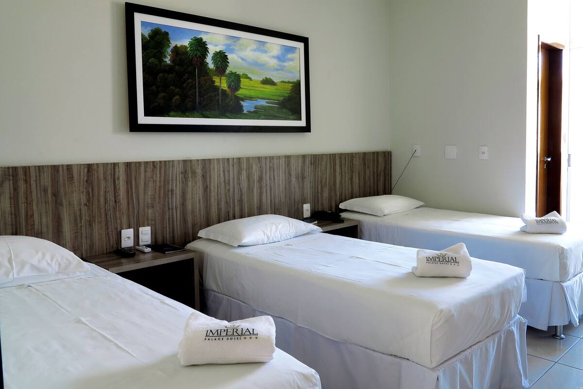 Ein Hotelzimmer mit zwei Betten, einem Holzkopfteil, einem Landschaftsbild und einer Tür rechts.