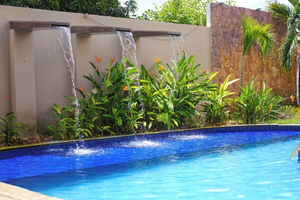 Una piscina con una fuente acuática, rodeada de plantas y un muro de piedra.
