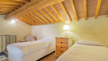 Ein Schlafzimmer mit zwei Betten, Holzbalken, einem Nachttisch mit Lampe und einem Sessel.