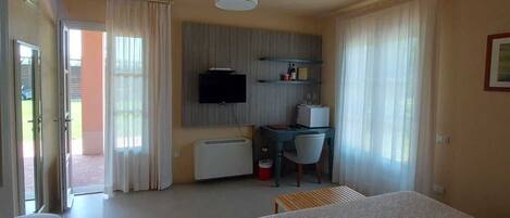 Una habitación de hotel con una cama grande, un escritorio con una silla, un televisor y una ventana con cortinas.