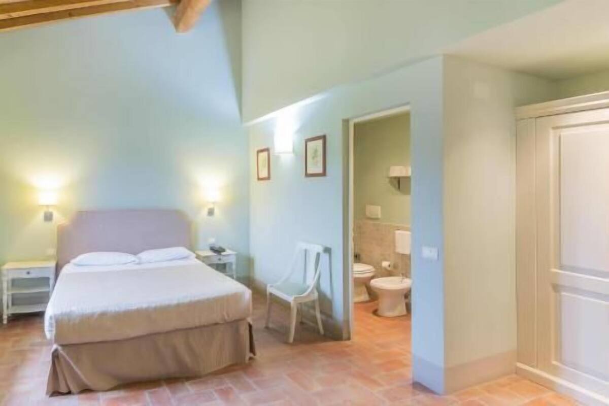 A bedroom with a bed, bedside tables, a chair, and a bathroom with a toilet and sink.
