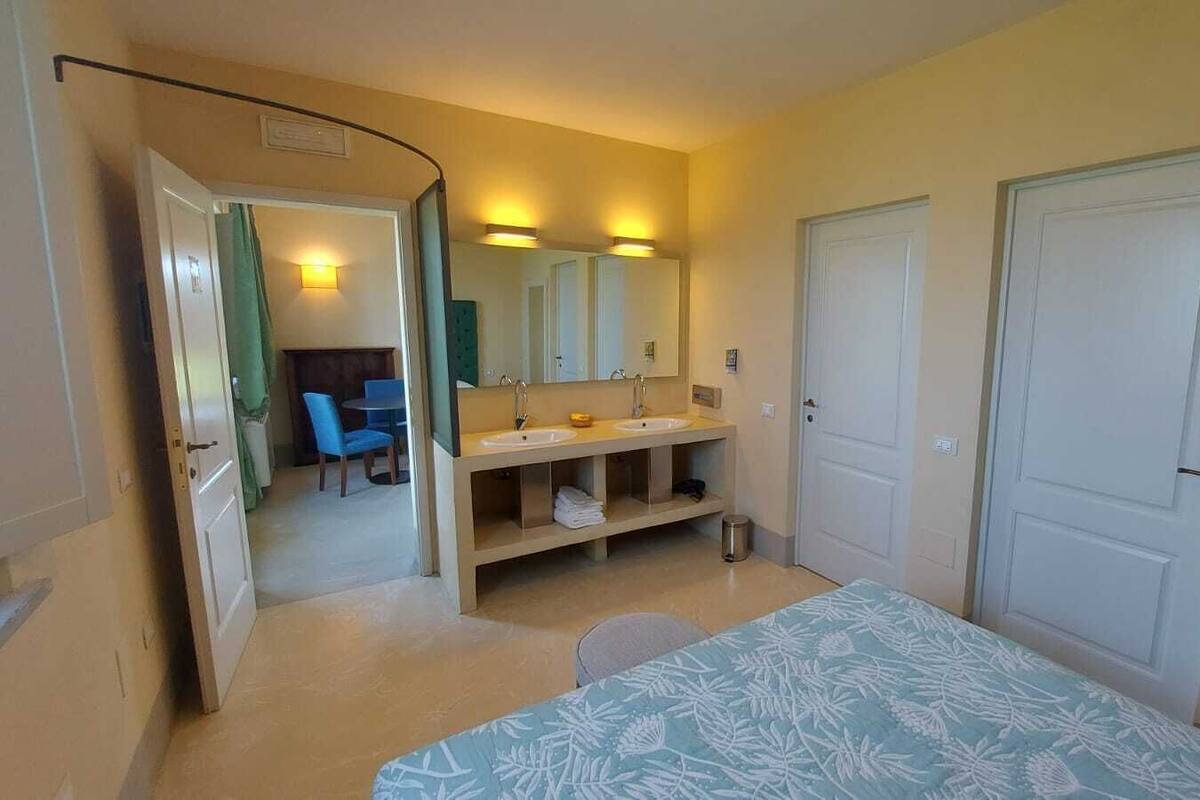 A hotel room with a bed, a bathroom with a sink and mirror, and a door leading to another room.