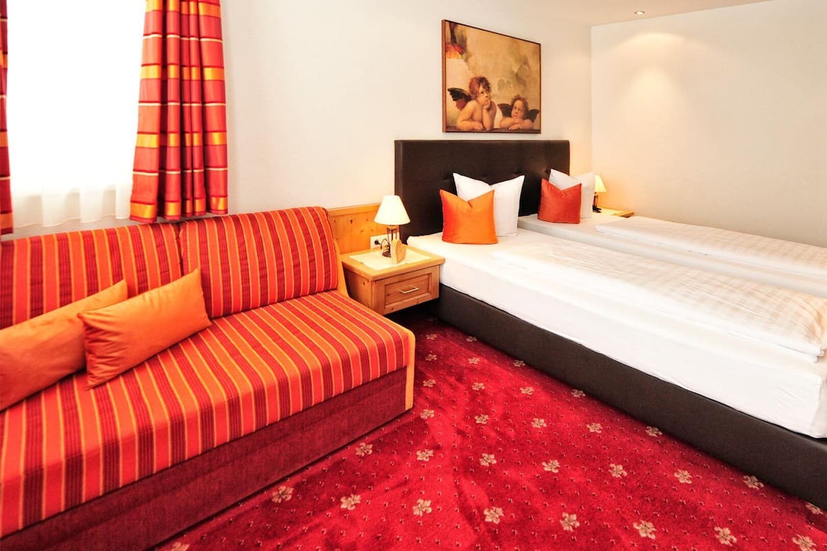 A hotel room with a striped sofa, a bed with white bedding, and a red carpet.