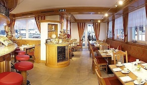 A restaurant with wooden furniture, a bar area, and large windows. - Hotel Garni Alpenstern (Ischgl)