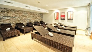 A spa room with multiple reclining chairs, a stone wall, and three framed artworks on the wall. - Hotel Garni Alpenstern (Ischgl)