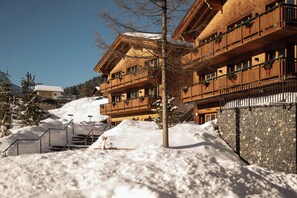 A multi-story wooden building with balconies, a stone wall, and a snow-covered slope.