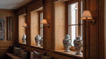 A room with wooden paneled walls, large windows with wall-mounted lamps, and a bench with cushions.