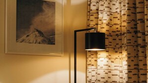 A hotel room with a bed, a framed picture of a mountain, a lamp, and patterned curtains. - Hotel Aurelio (Lech am Arlberg)