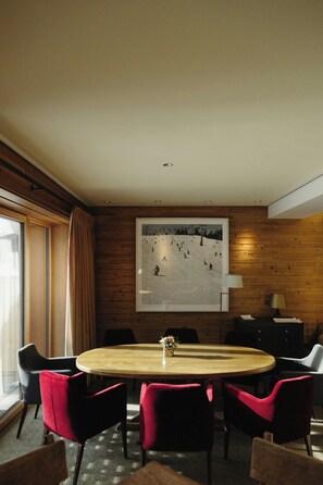 A conference room with a round table, red chairs, a large framed picture of a ski slope, and wooden paneling on the walls. - Hotel Aurelio (Lech am Arlberg)