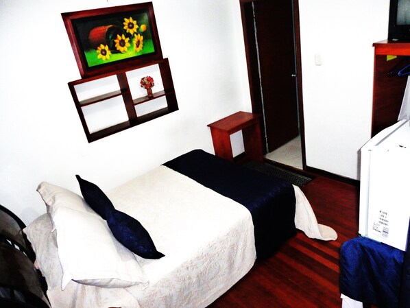 A hotel room with a bed, a small wooden nightstand, a mirror, and a television mounted on the wall.