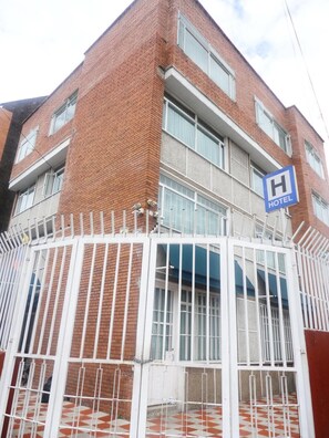 A hotel with a brick facade, a gated entrance, and a blue 'H' sign indicating the hotel.