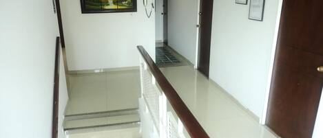 Un pasillo limpio y bien iluminado con una escalera, un cuadro enmarco de un paisaje y una puerta con el número 25.