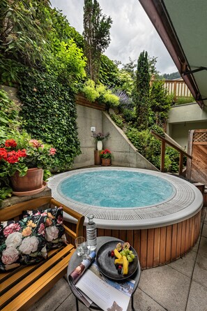 A hot tub surrounded by lush greenery, a wooden bench, and a table with fruit and a drink. - Alpin Resort Stubaierhof (Fulpmes)
