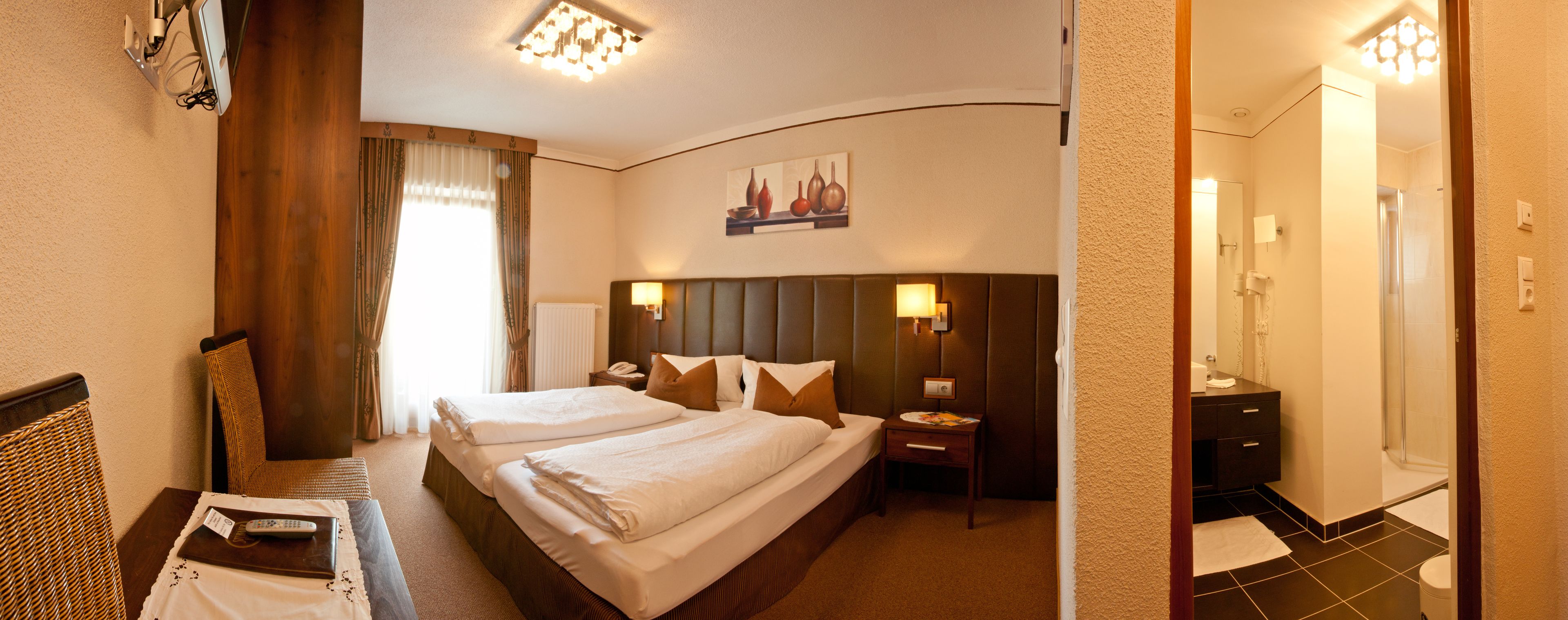 A hotel room with two beds, a desk, a chair, a nightstand, and a painting on the wall.