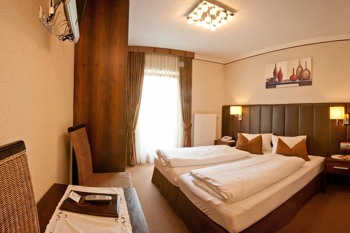 Une chambre d’hôtel avec deux lits, un bureau, une chaise, un tableau et une salle de bain avec douche.