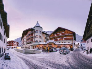 Un hotel con una torre central, varios balcones y una calle cubierta de nieve.