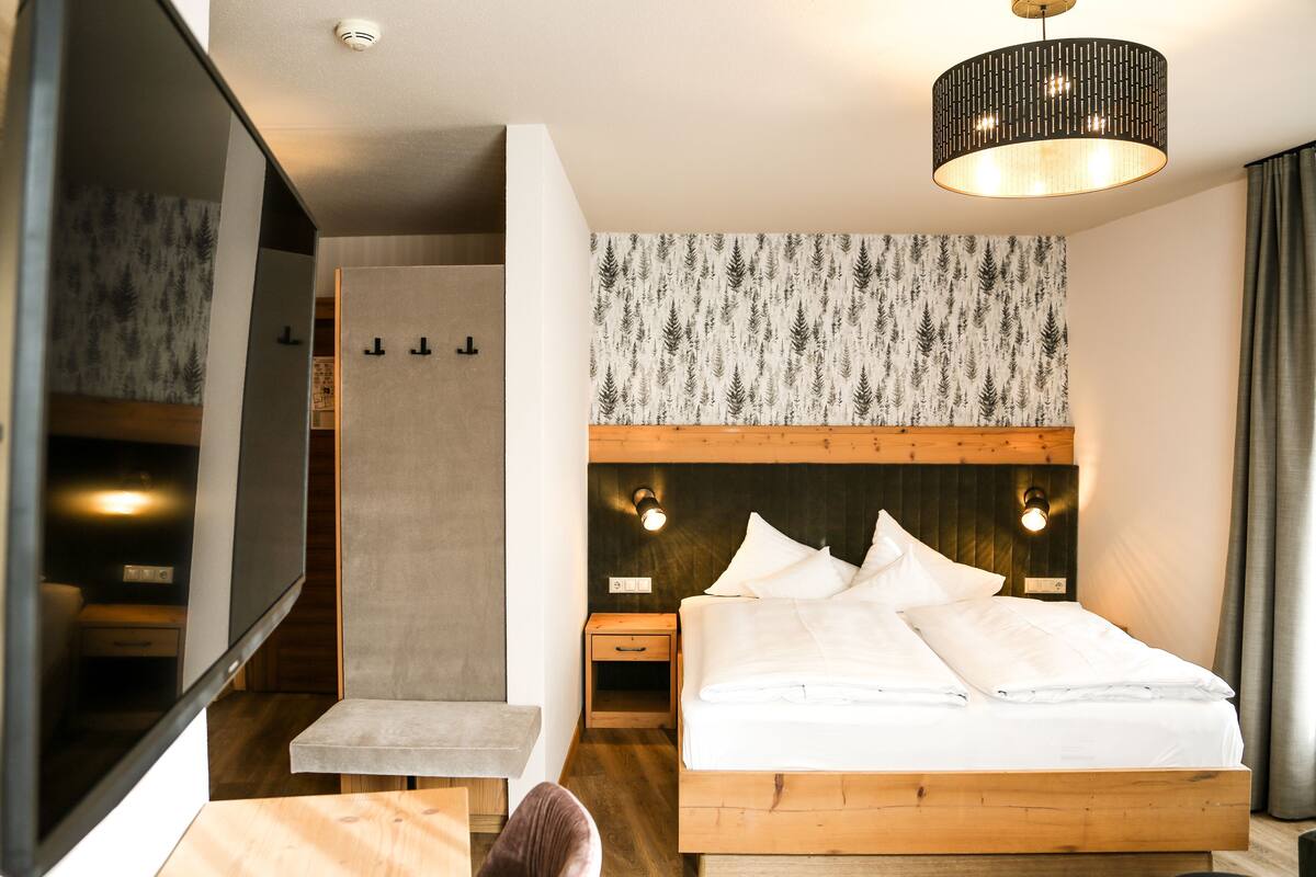 Une chambre d’hôtel moderne avec un grand lit, une tête de lit en bois, un luminaire fixé au mur et un miroir.