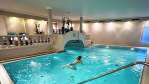 An indoor swimming pool with clear water, a diving board, and a person swimming. - Alpin Resort Stubaierhof (Fulpmes)