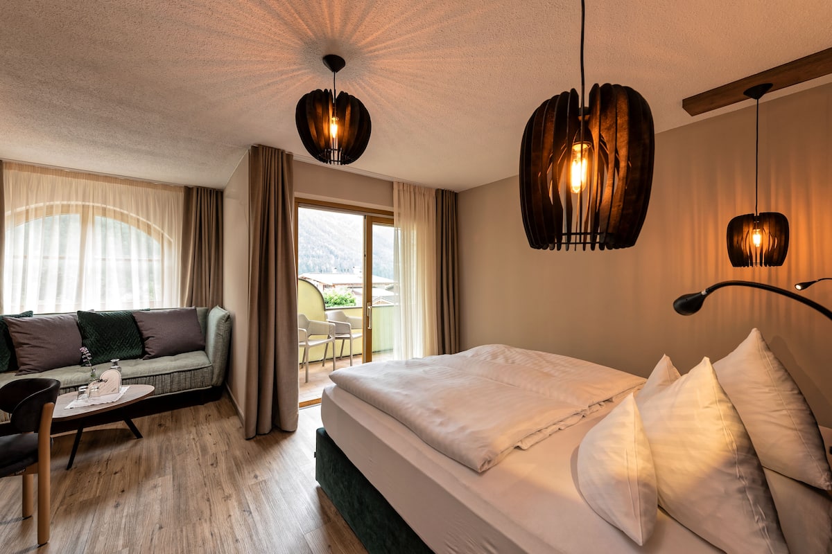 Une chambre d’hôtel avec un lit, un canapé, une petite table et un balcon avec une chaise.