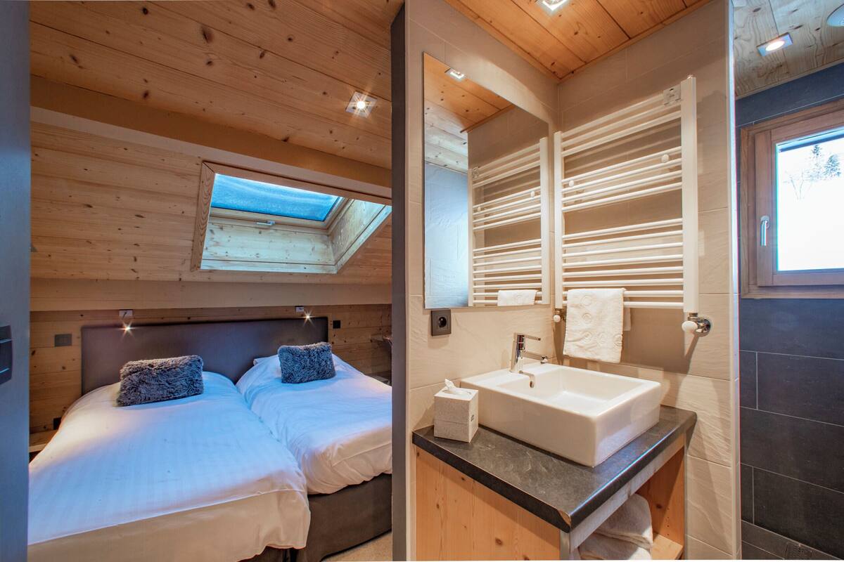 A bedroom with two beds, a skylight, and a bathroom with a large sink and mirror.