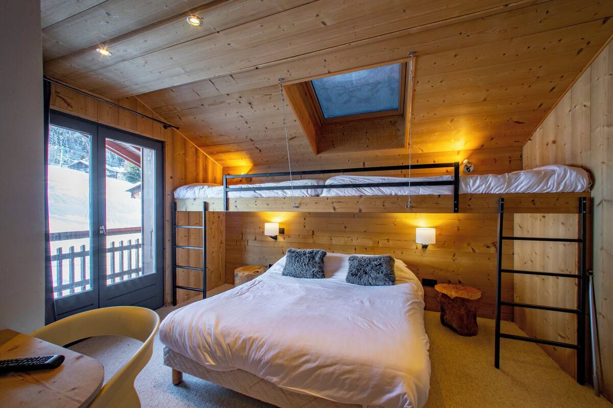 A wooden cabin bedroom with bunk beds, a skylight, and a view of a snowy landscape.