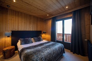A wooden-paneled bedroom with a large bed, a nightstand, and a window with curtains.