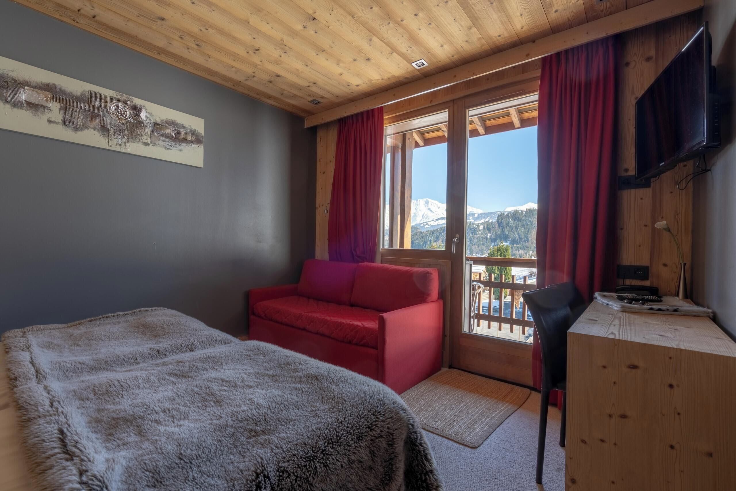 Una habitación con techo de madera, cama, sofá rojo, escritorio y televisor.