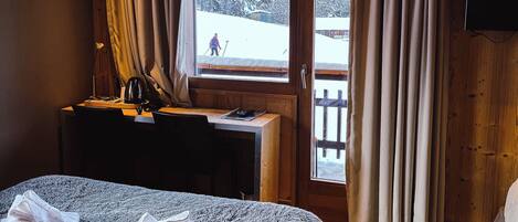 Una habitación de hotel acogedora, con techo de madera, una cama grande, un escritorio con silla y una ventana con cortinas.