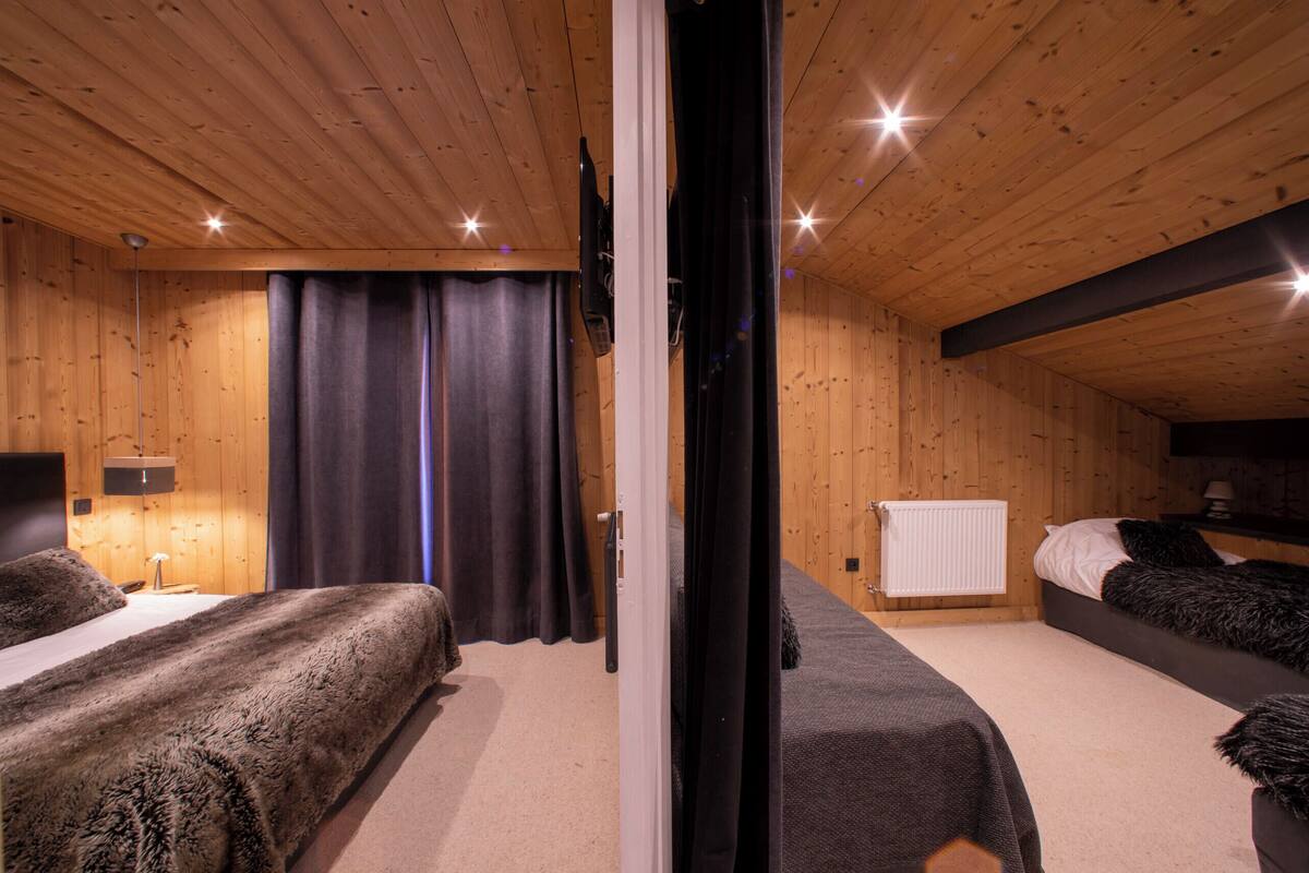 A wooden-paneled room with two beds, a radiator, and a television mounted on the wall.