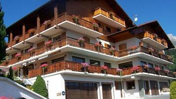 Un hotel de varios pisos con balcones decorados con flores, fachada blanca y montañas al fondo.