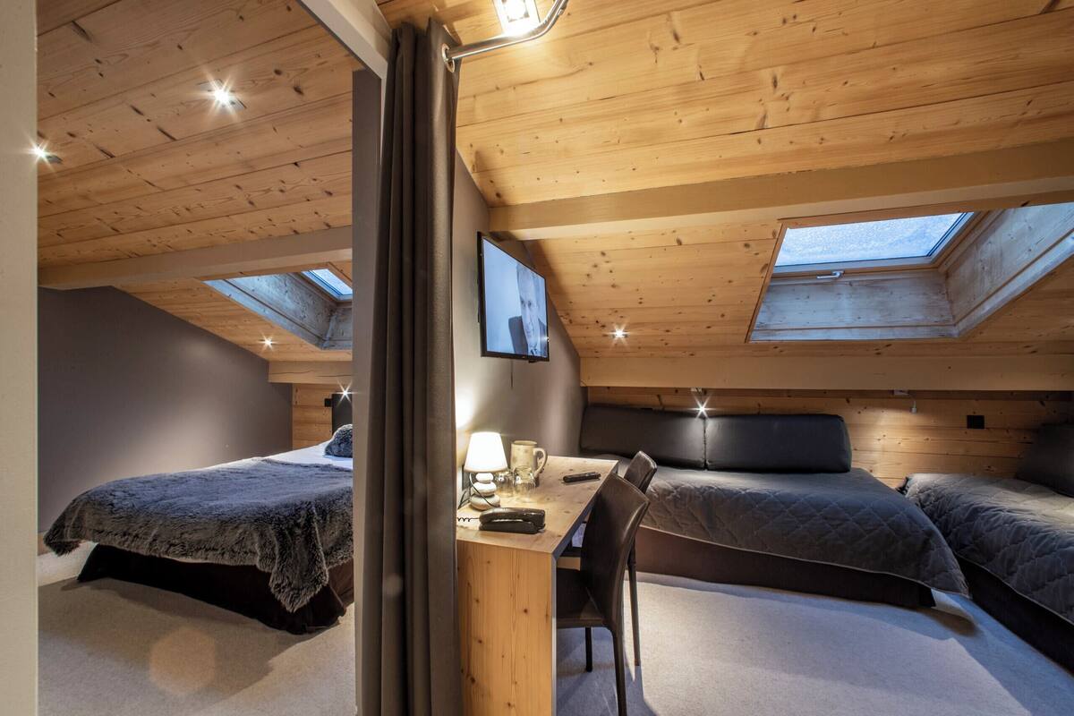A bedroom with two beds, a desk, and a TV. There are skylights on the ceiling.