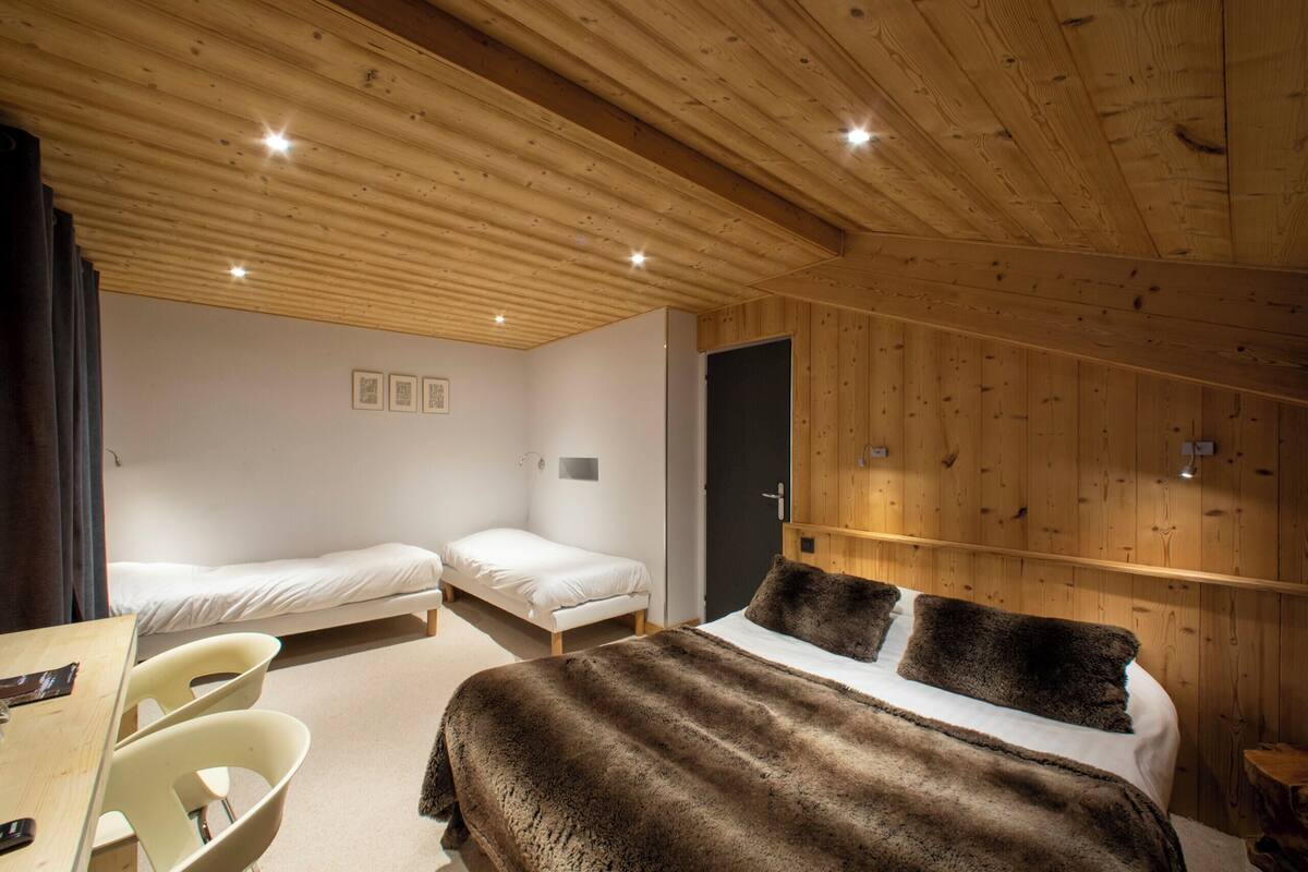 A room with two single beds, a larger bed with a fur throw, wooden walls, and a wooden ceiling.
