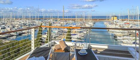 Un balcon donnant sur une marina remplie de bateaux, une table avec un chapeau et une serviette.