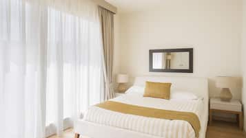 Una camera d'albergo con un letto grande, due comodini con lampade, uno specchio a parete e tende leggere.