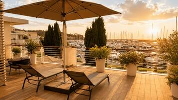 Een balkon met twee loungesteunen, een parasol en plantenpotten.
