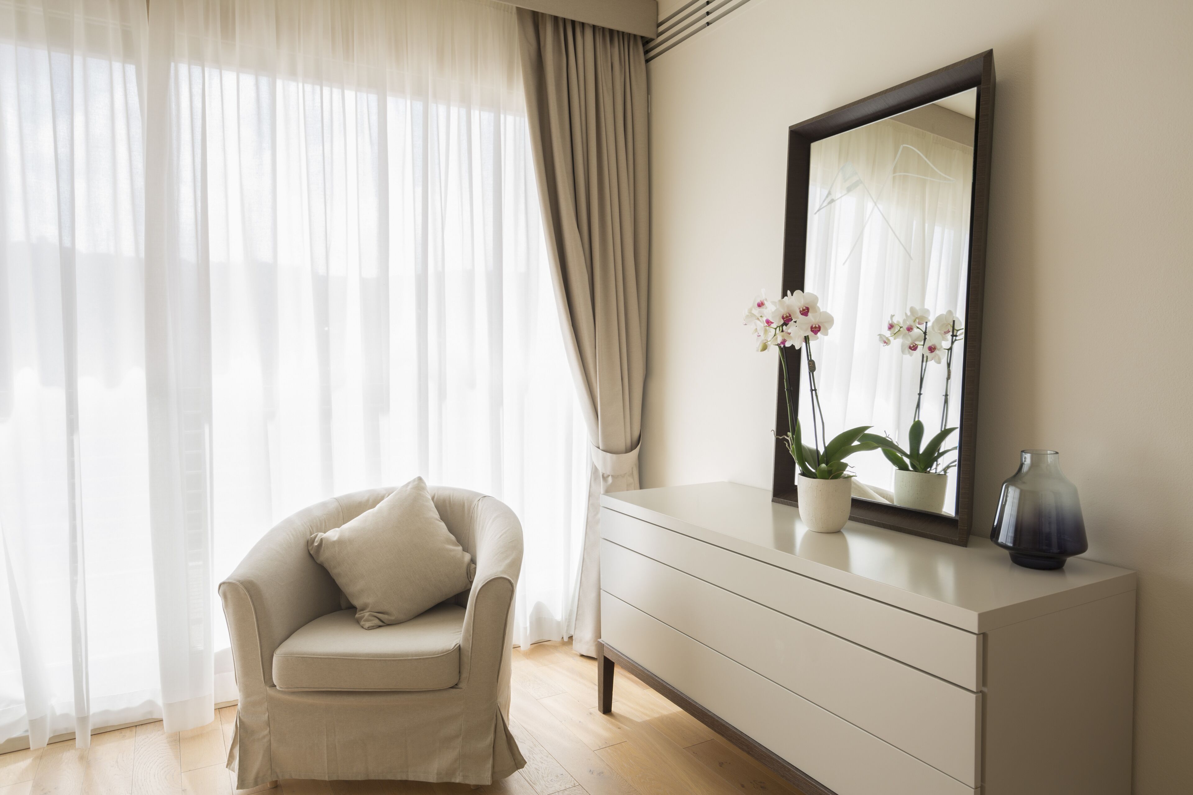 Une pièce avec un canapé de couleur claire, une commode, un miroir et une plante en pot.
