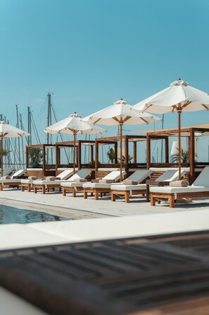 A poolside area with wooden lounge chairs and white umbrellas. - Marina di Scarlino Resort (Scarlino)