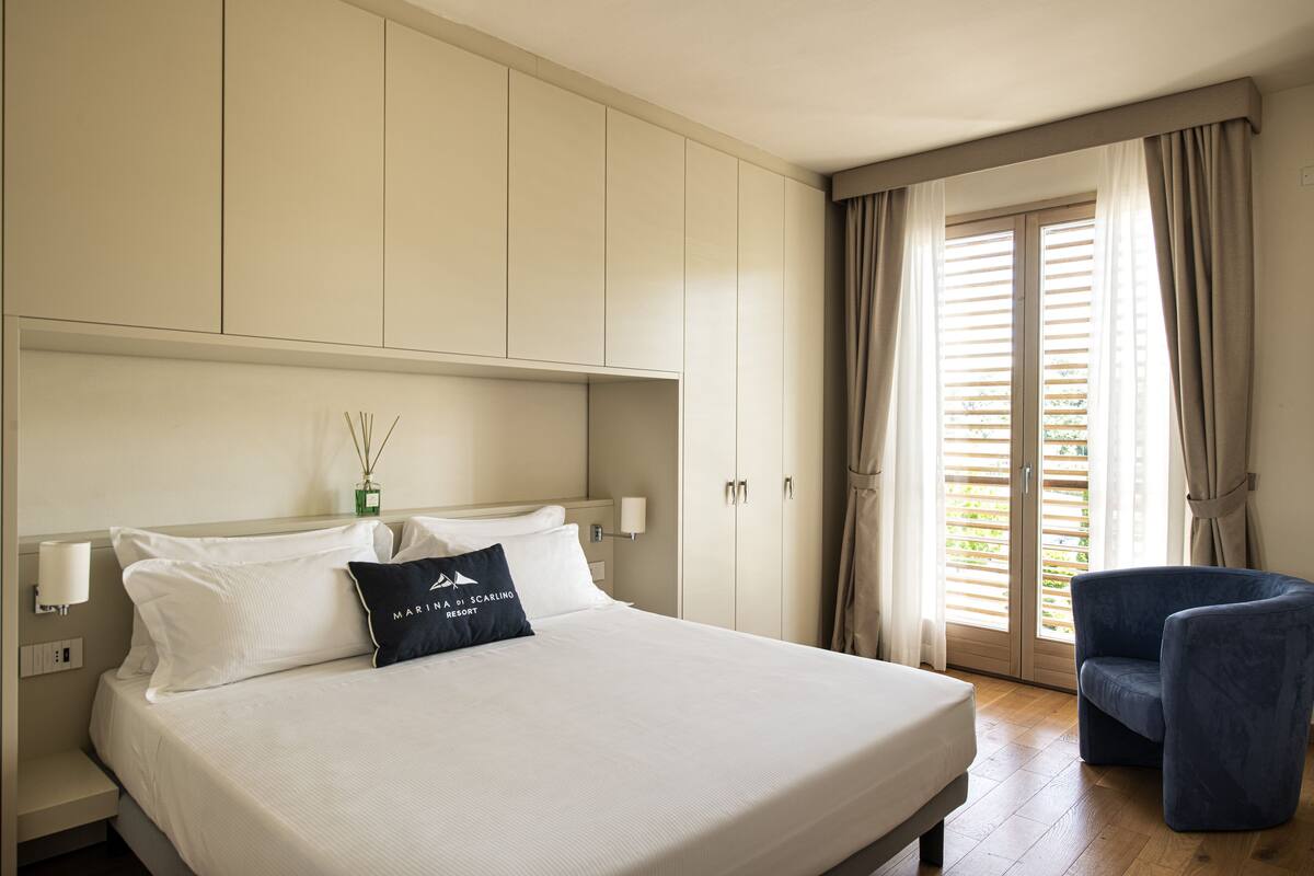 A hotel room with a large bed, a chair, a wardrobe, and a window with curtains.