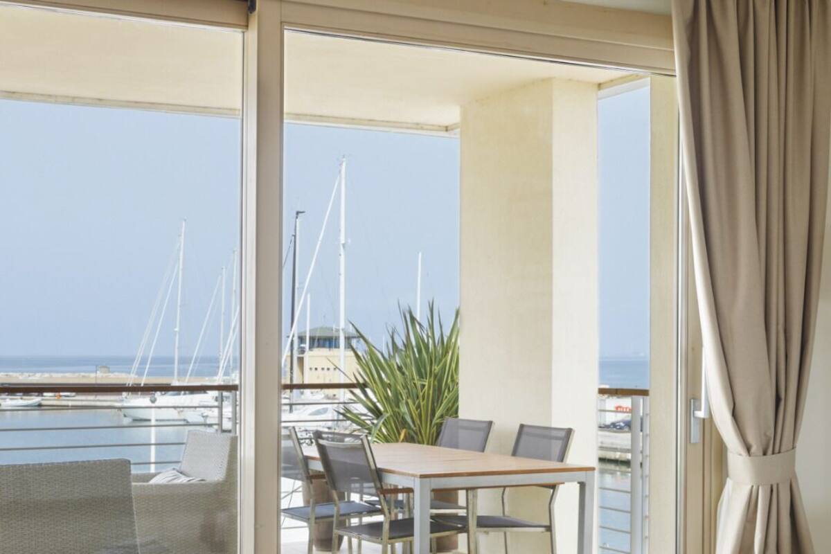 A balcony with a table, chairs, a plant, and a view of the marina.