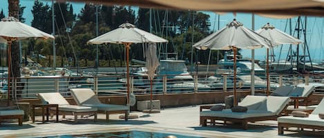 A pool area with lounge chairs and umbrellas, surrounded by a marina with boats.