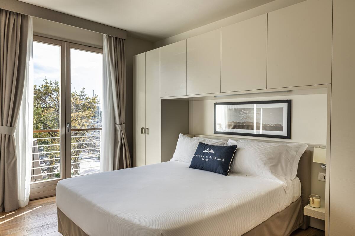 A hotel room with a large bed, a nightstand with a lamp, and a window with curtains.