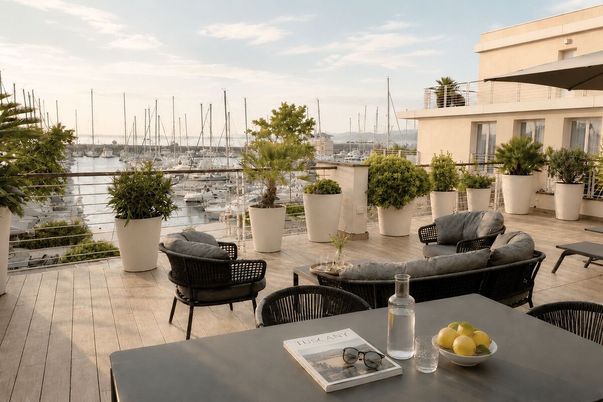A rooftop terrace with outdoor seating, potted plants, and a view of a marina.