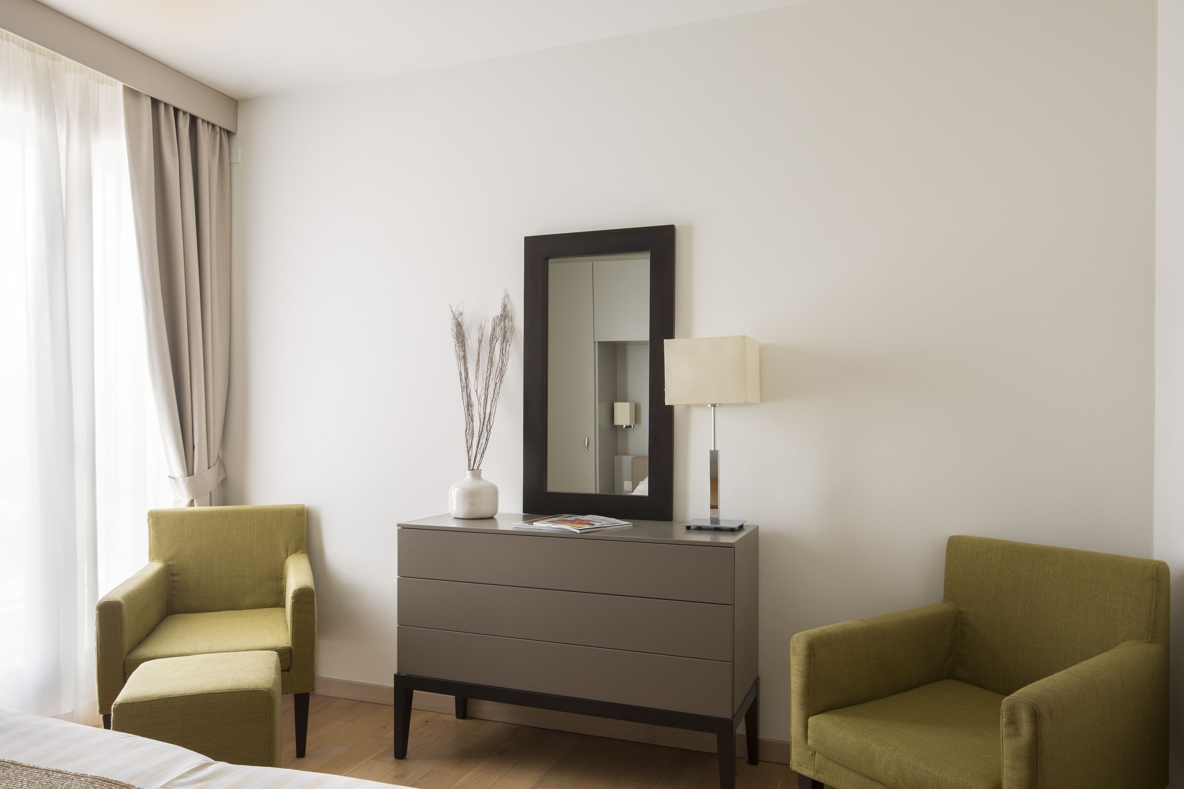 Una camera d'albergo con un letto, due poltrone, un comò, uno specchio e una lampada.