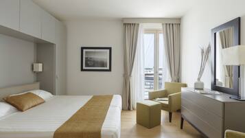 Une chambre d’hôtel avec un lit, un bureau, une chaise, une commode et une fenêtre avec des rideaux.