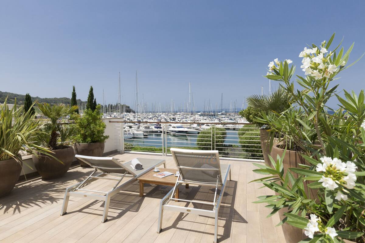 A terrace with lounge chairs and potted plants overlooking a marina with numerous boats.