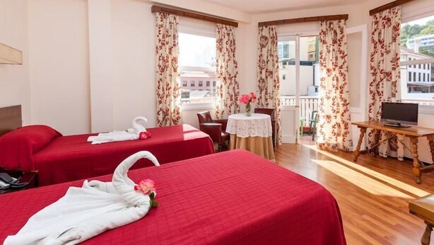 Een hotelkamer met twee bedden, een klein balkon, een televisie en een tafel met een bloevas.