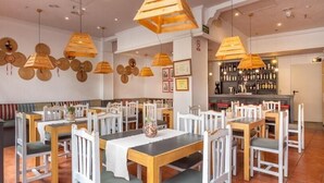 Een restaurant met houten tafels en stoelen, hangende houten lampen, en een bar met flessen op planken.