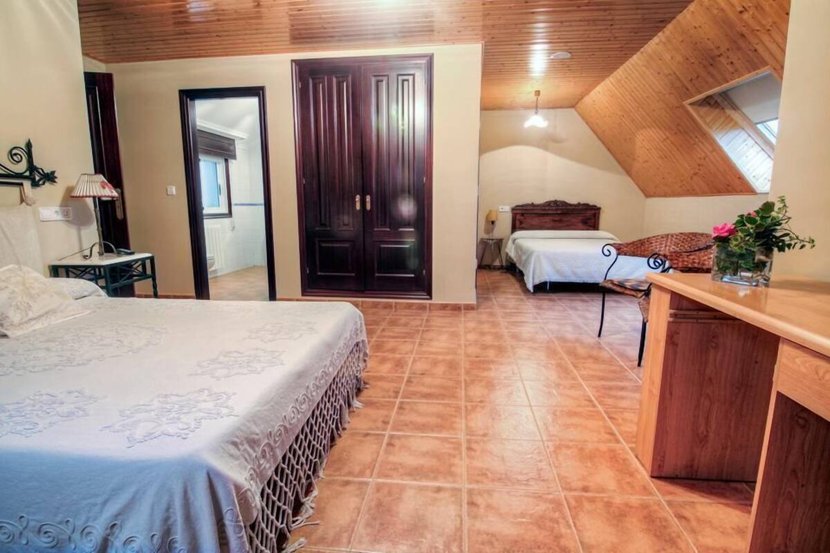 A bedroom with a large bed, a wooden desk, and a small table with a lamp.